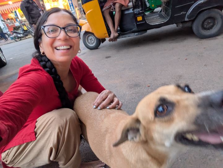Lekshmi crouching beside a friendly street dog next to an autorickshaw