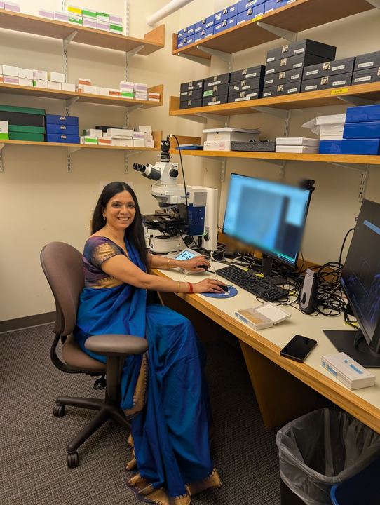 Lekshmi in a sari working at a microscope workstation